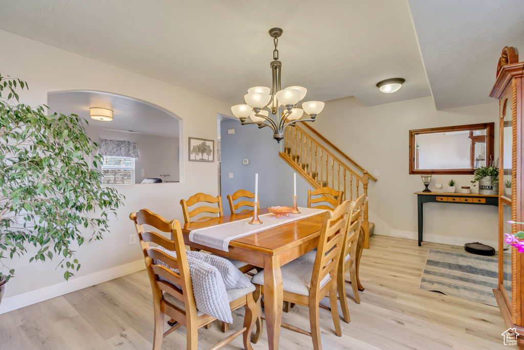 Dining area with baseboards, light wood finished floors, an inviting chandelier, arched walkways, and stairs