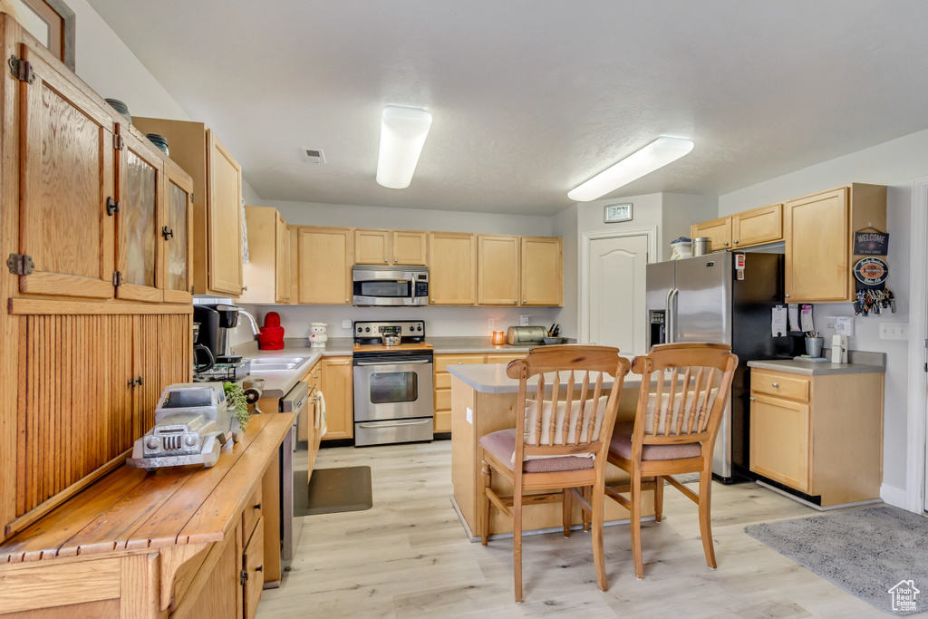 Kitchen with light brown cabinets, a kitchen island, light wood-type flooring, stainless steel appliances, and a sink