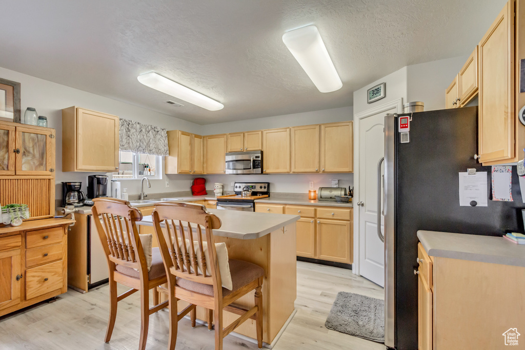Kitchen with a breakfast bar, light wood-style floors, appliances with stainless steel finishes, and light brown cabinetry