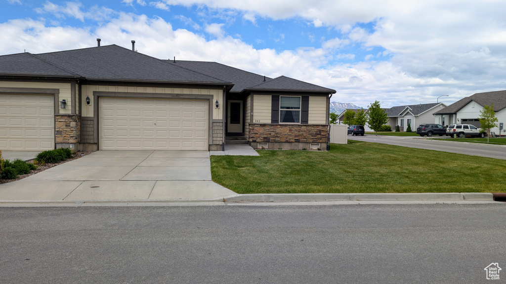 View of front of property with stone siding, a front lawn, driveway, a garage, and a residential view