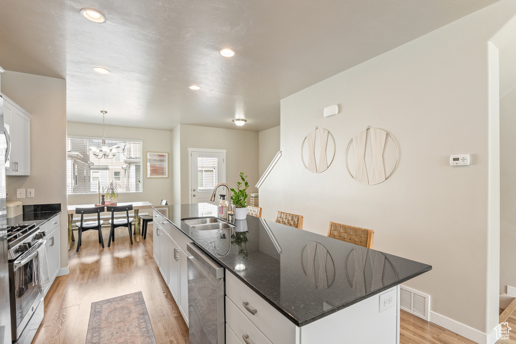 Kitchen featuring appliances with stainless steel finishes, light wood-style flooring, a sink, white cabinetry, and an island with sink