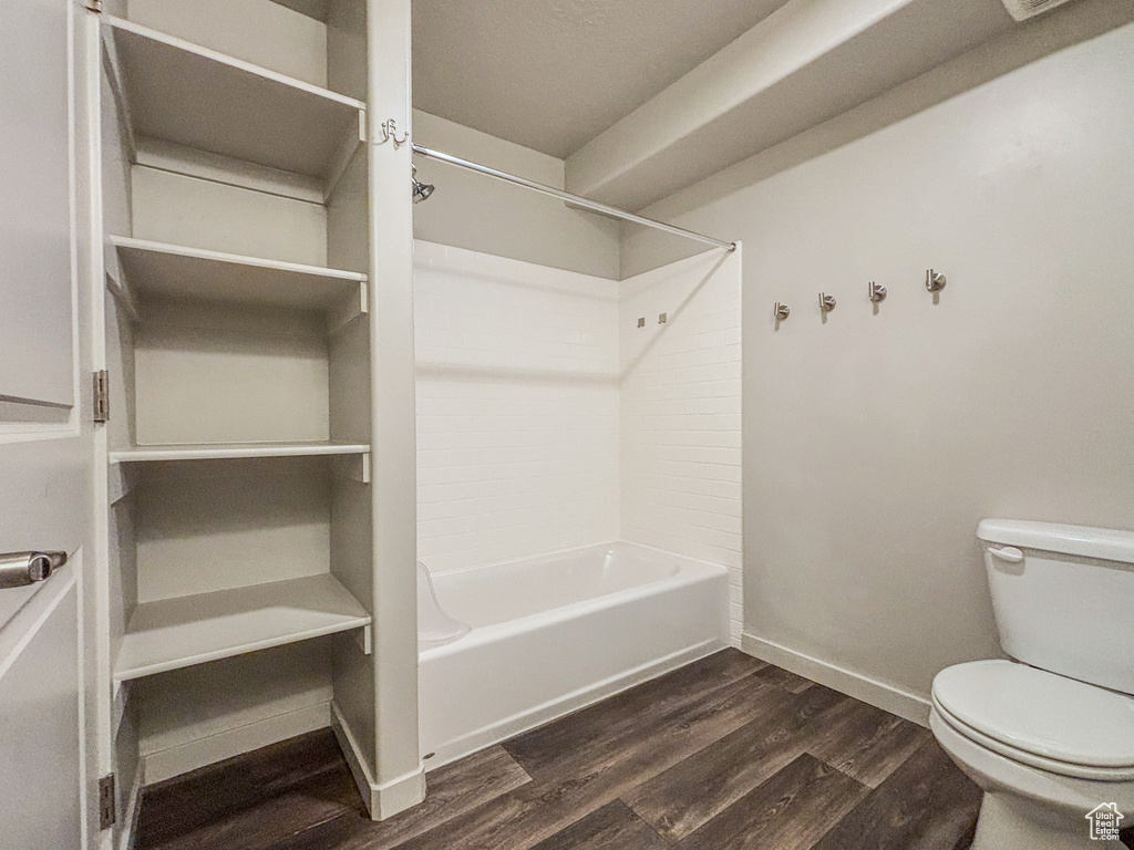 Bathroom with bathing tub / shower combination, toilet, wood finished floors, and baseboards
