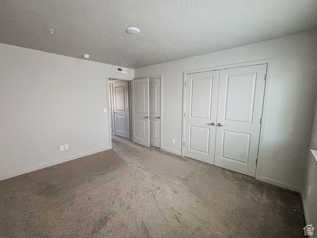 Unfurnished bedroom featuring visible vents, baseboards, carpet, multiple closets, and a textured ceiling
