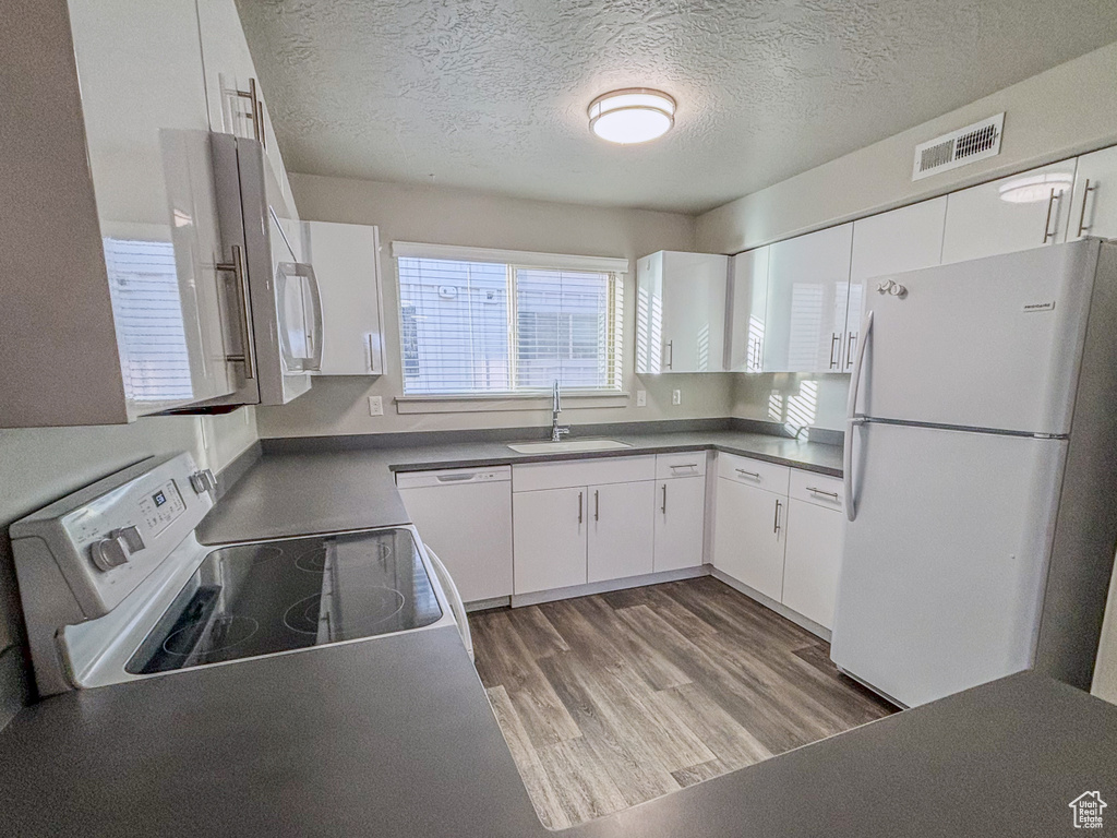 Kitchen with dark countertops, visible vents, light wood-style floors, white appliances, and a sink