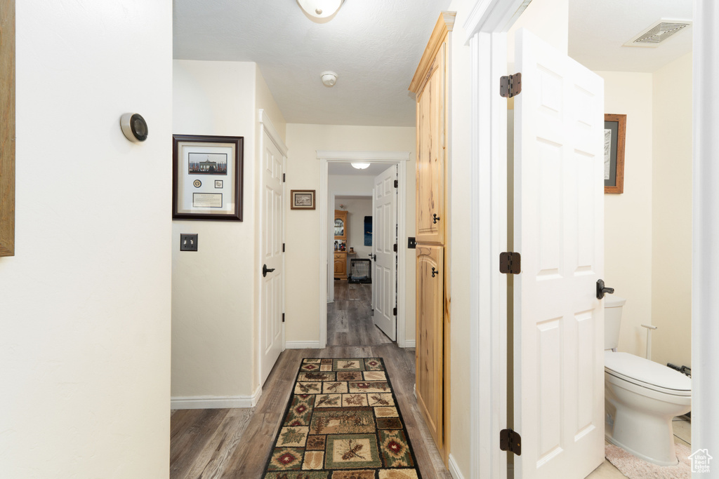 Corridor with wood finished floors, visible vents, and baseboards