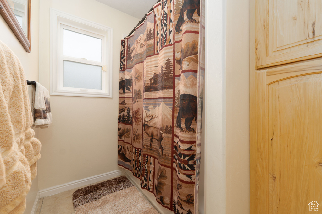 Bathroom with curtained shower, baseboards, and tile patterned flooring
