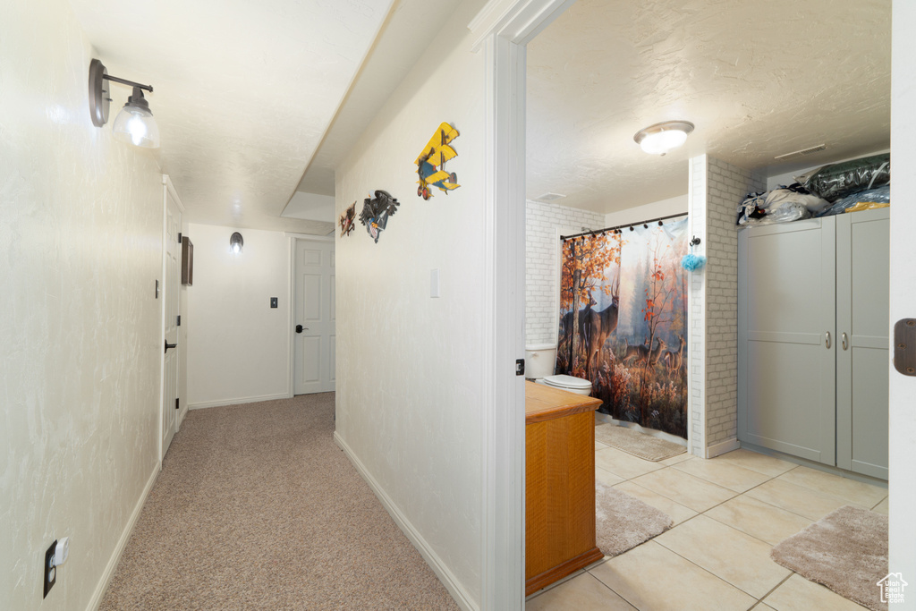 Corridor with light tile patterned floors, a textured ceiling, and baseboards