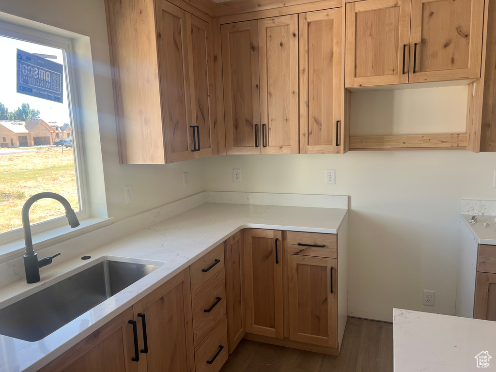 Kitchen featuring a sink, light stone counters, and wood finished floors