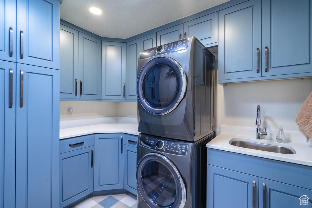 Washroom with a sink, cabinet space, stacked washer and clothes dryer, and recessed lighting