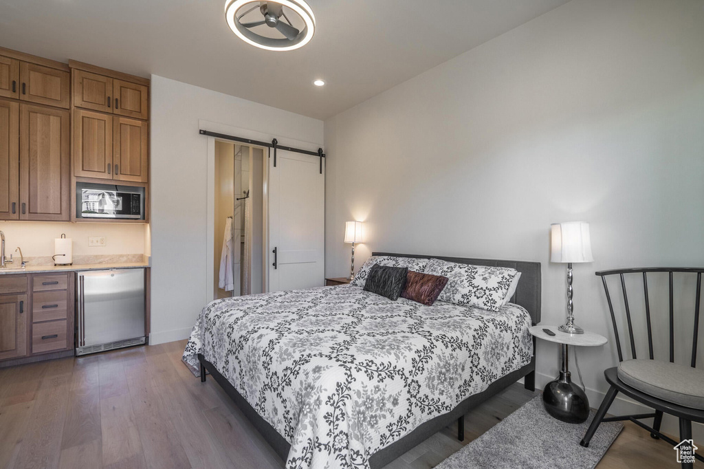 Bedroom with baseboards, a barn door, recessed lighting, wood finished floors, and stainless steel fridge
