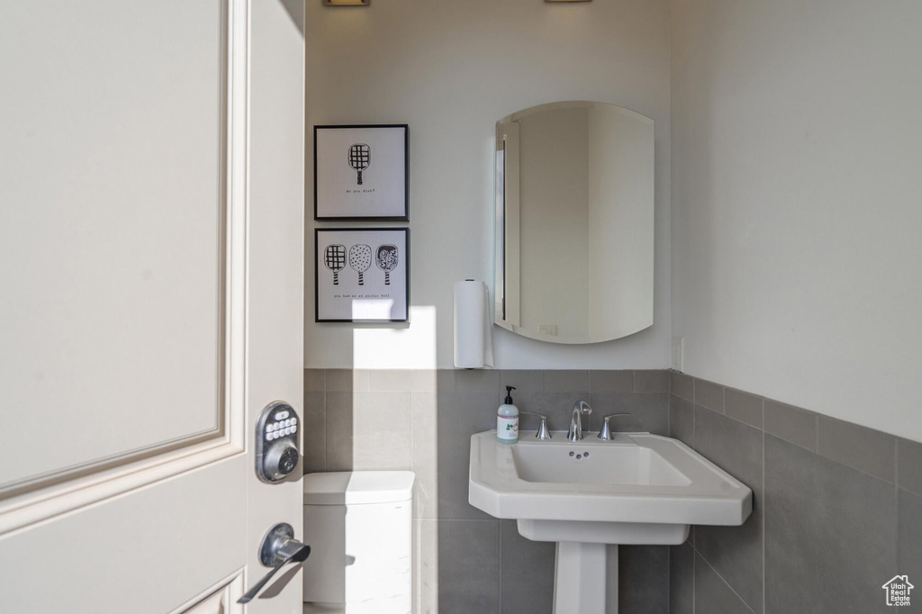 Half bath featuring a sink, toilet, tile walls, and wainscoting