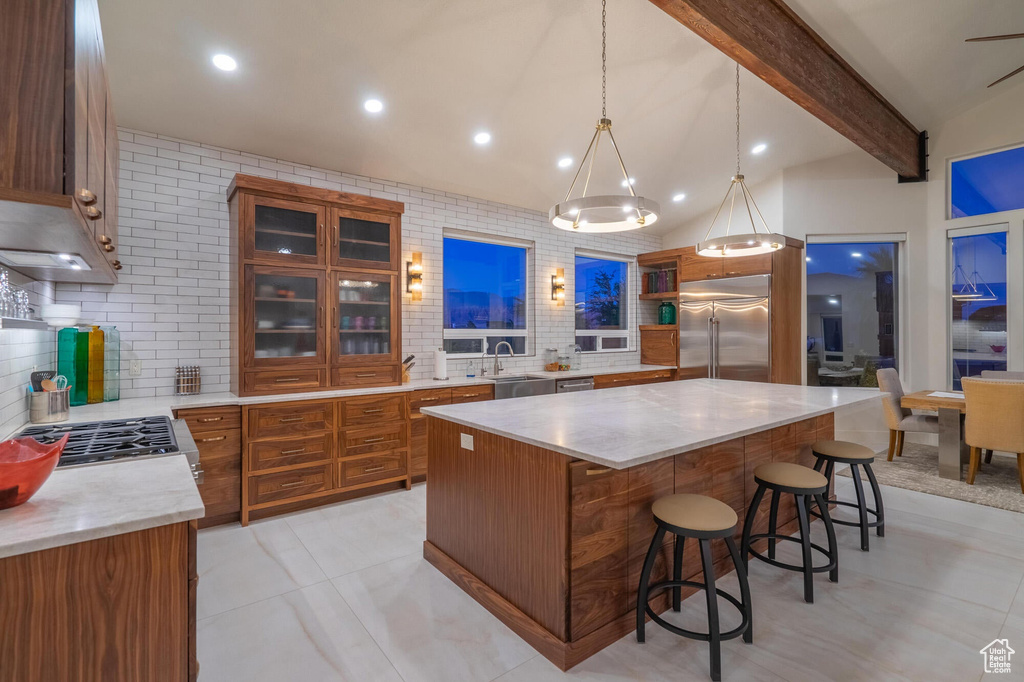 Kitchen with a kitchen bar, stainless steel built in refrigerator, a sink, backsplash, and brown cabinetry