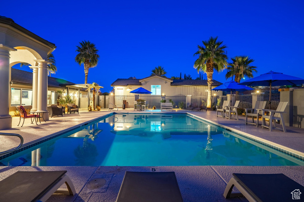 Pool at night featuring a fenced in pool, fence, and a patio area