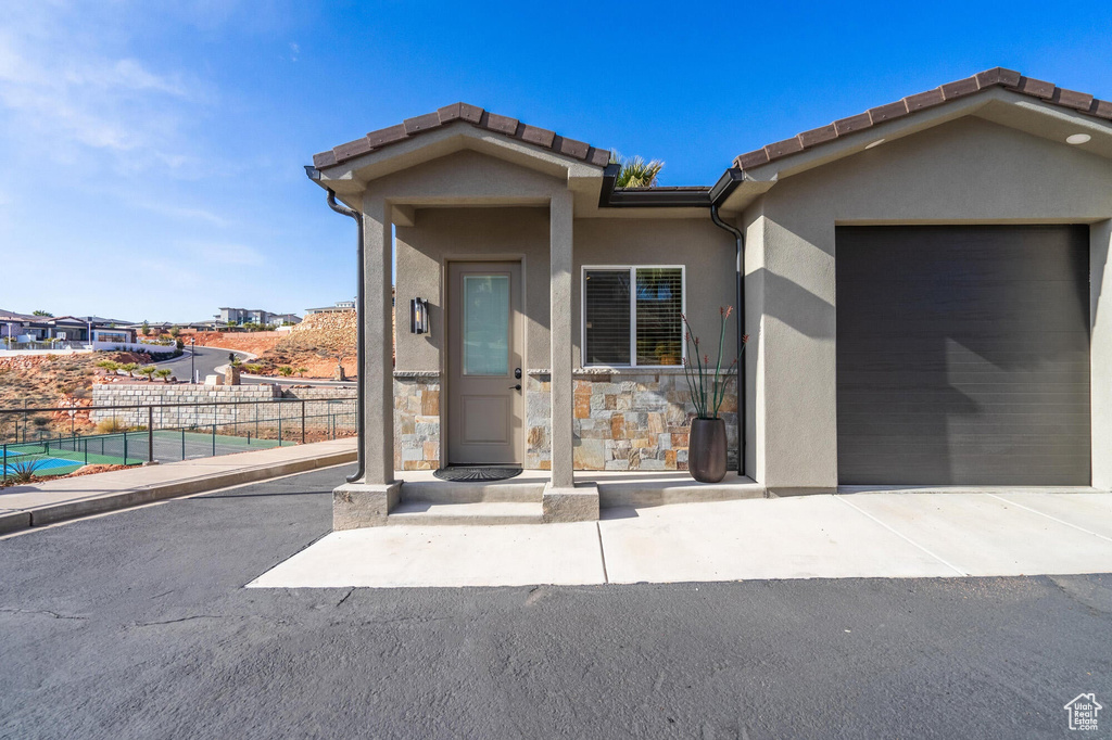 View of front of house with fence, stucco siding, a garage, stone siding, and a tile roof