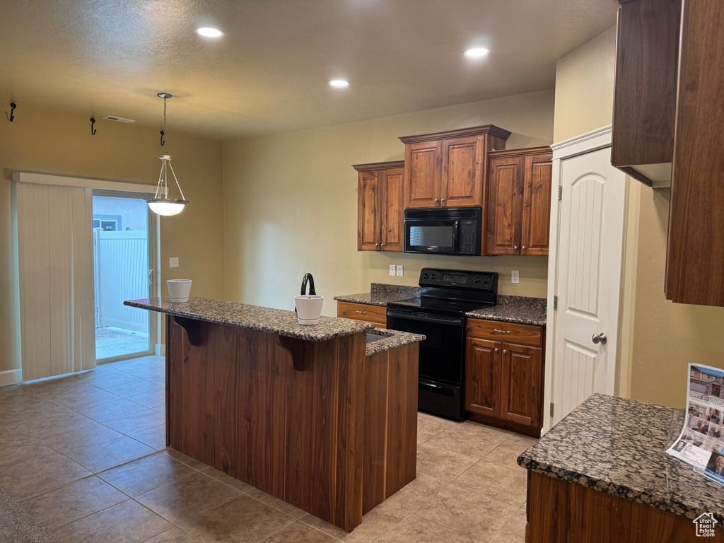 Kitchen featuring hanging light fixtures, a breakfast bar area, dark stone counters, black appliances, and a kitchen island