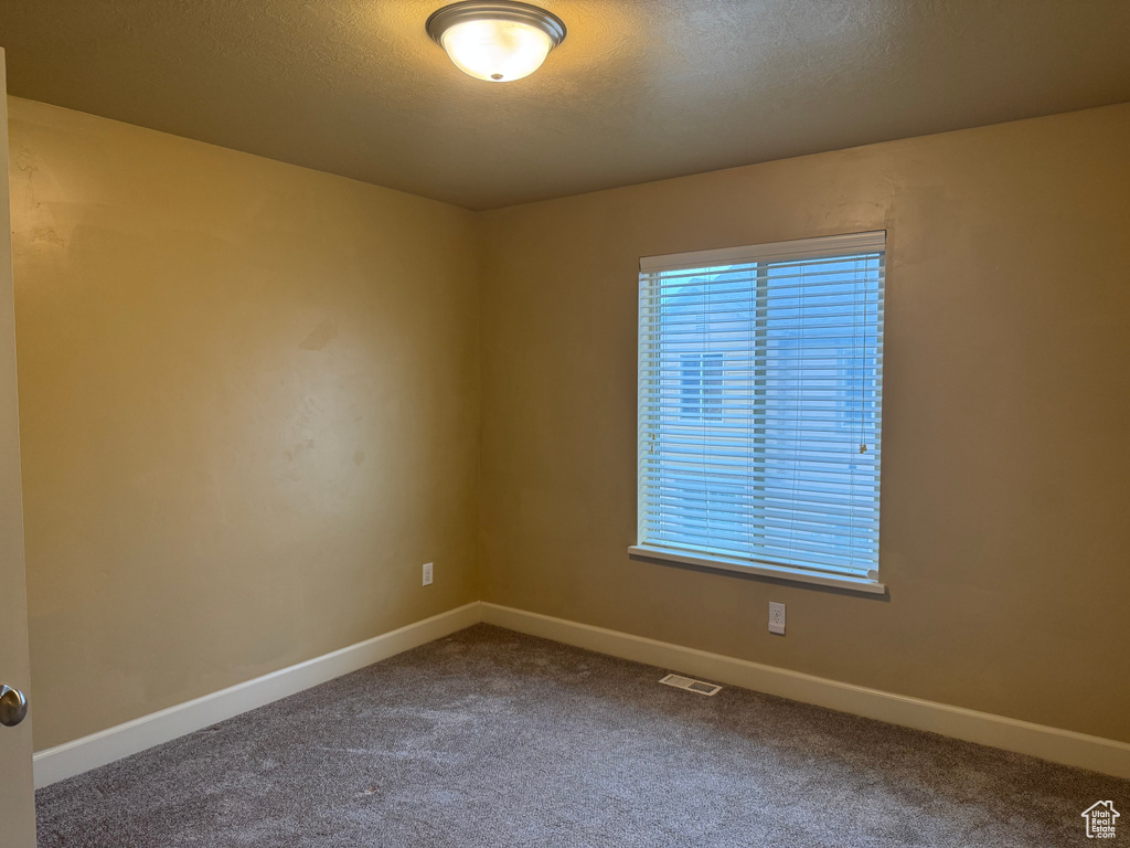Carpeted spare room featuring a textured ceiling, baseboards, and visible vents