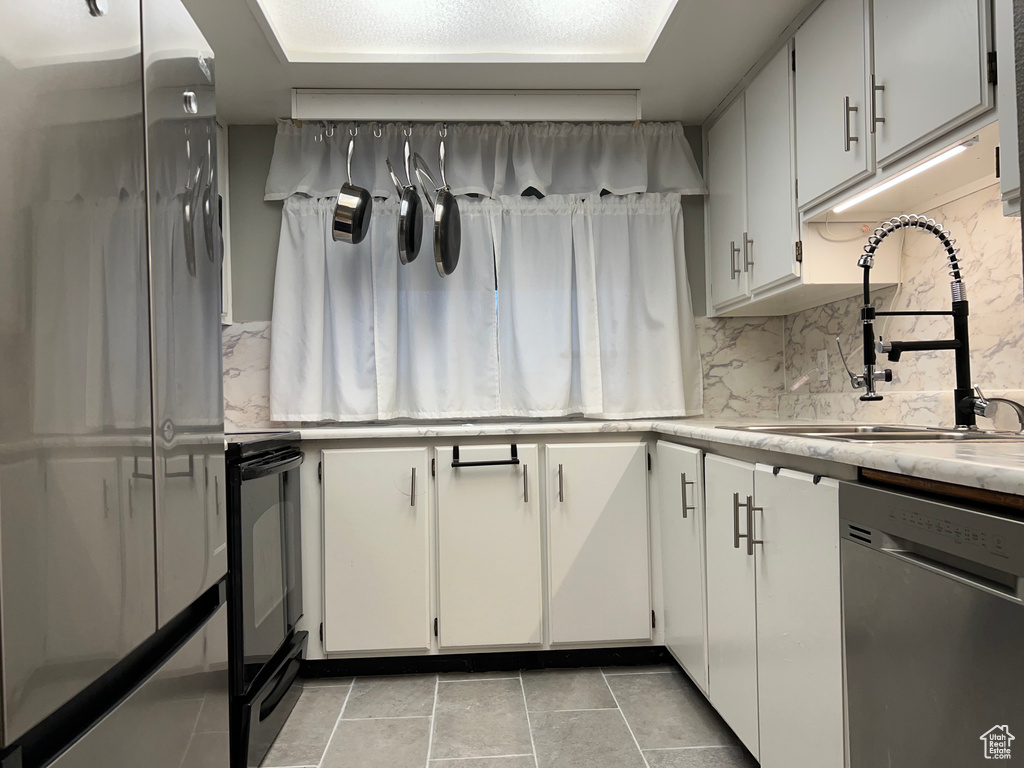 Kitchen featuring a sink, stainless steel appliances, light countertops, white cabinets, and tasteful backsplash