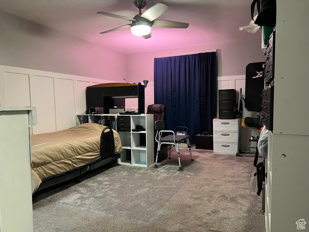 Bedroom featuring carpet flooring, wainscoting, a decorative wall, and a ceiling fan