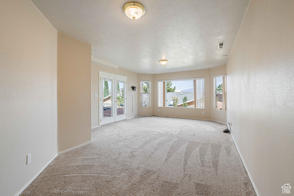 Carpeted spare room with visible vents, a textured ceiling, baseboards, and a textured wall