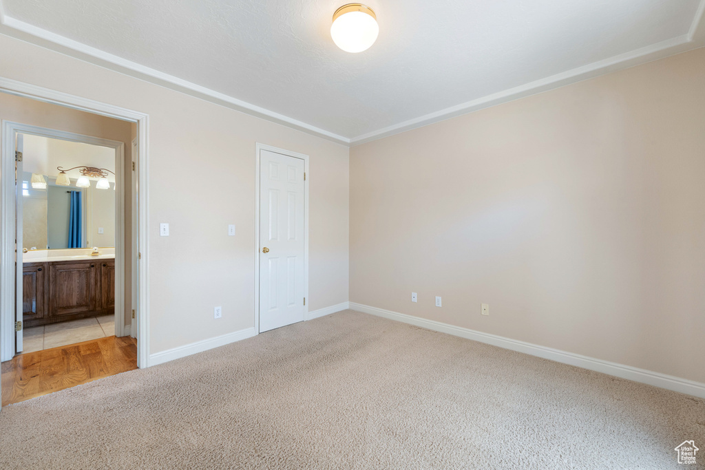 Unfurnished bedroom with ensuite bath, baseboards, and light carpet