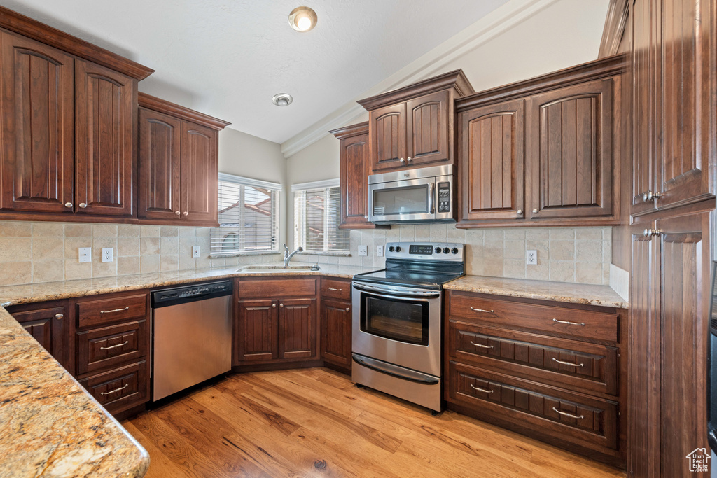 Kitchen featuring light stone counters, a sink, stainless steel appliances, vaulted ceiling, and light wood-type flooring