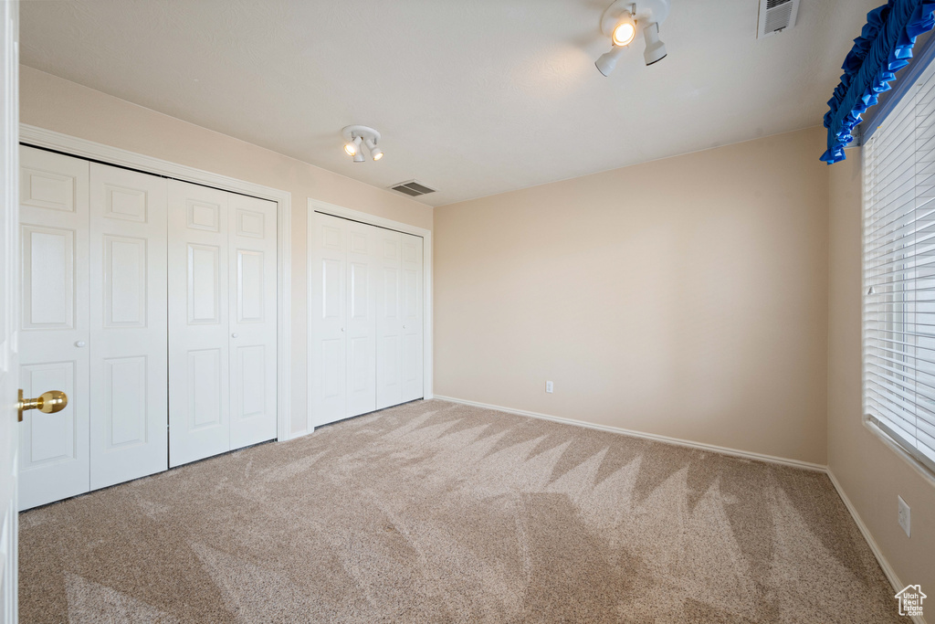 Unfurnished bedroom featuring visible vents, multiple closets, carpet, and baseboards