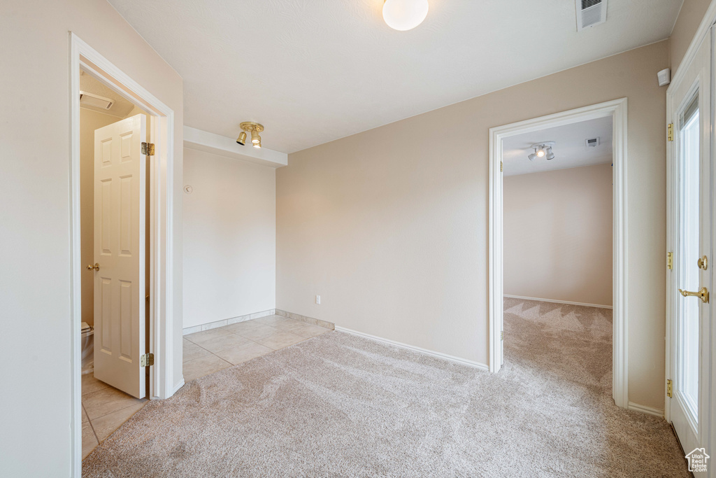 Empty room with light tile patterned flooring, light colored carpet, visible vents, and baseboards