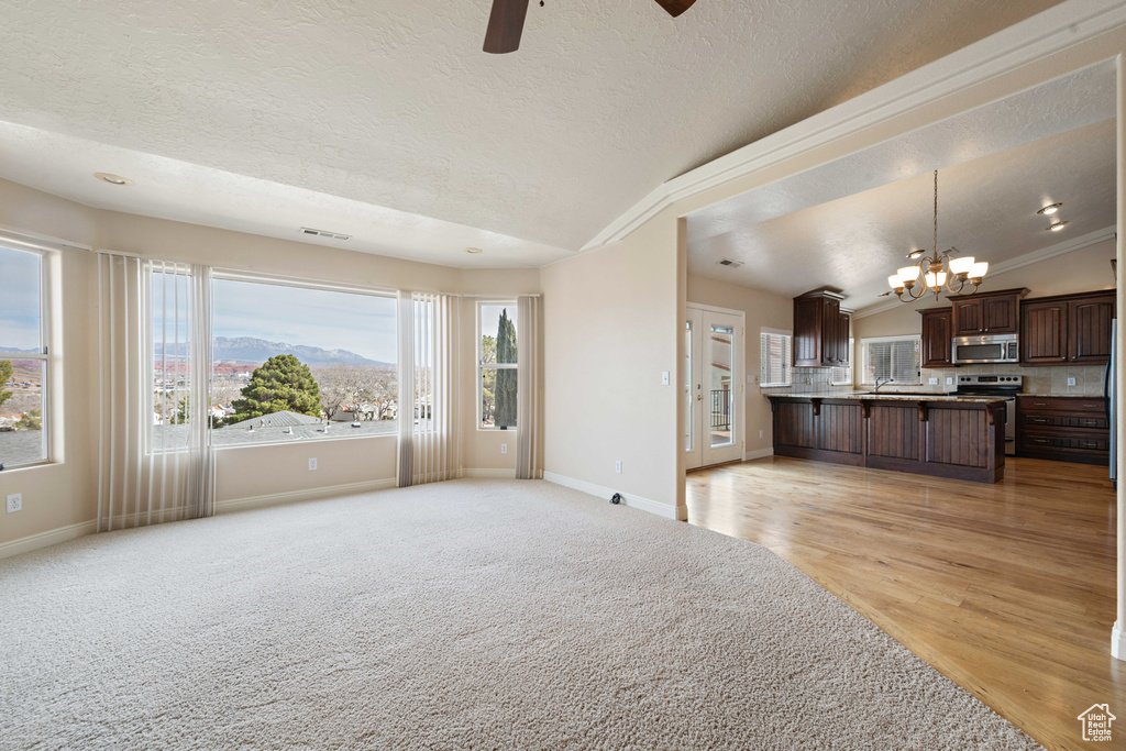 Unfurnished living room with baseboards, ceiling fan with notable chandelier, a textured ceiling, and vaulted ceiling