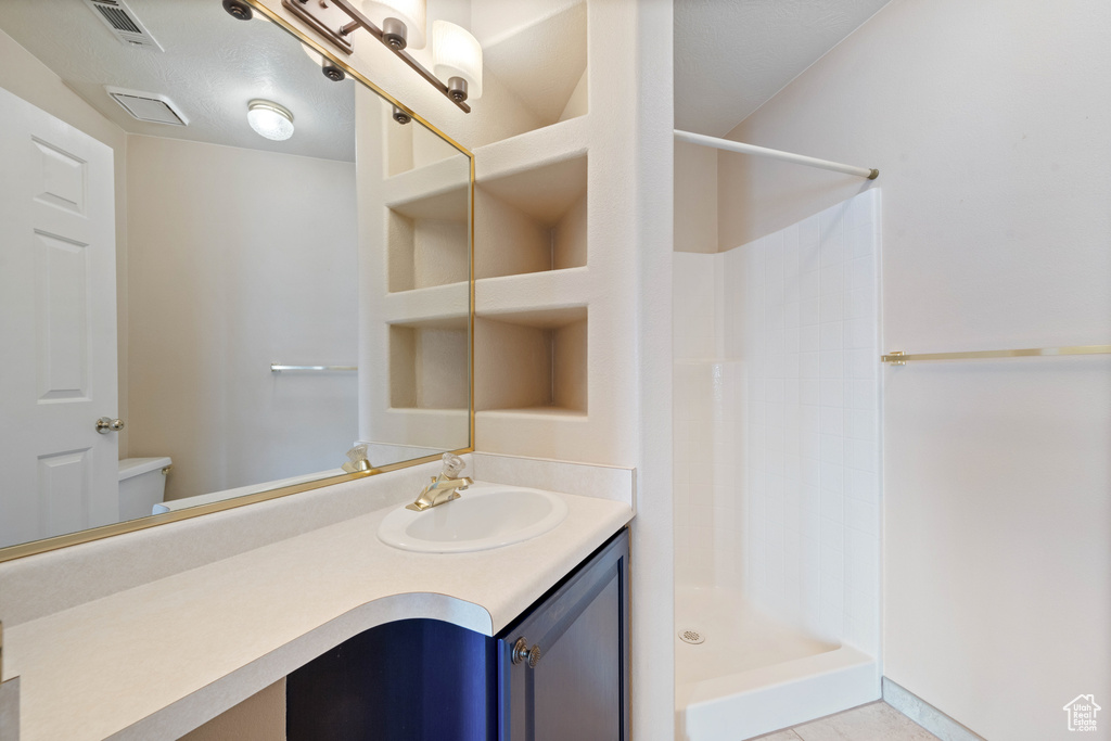 Full bathroom with tile patterned floors, visible vents, toilet, walk in shower, and vanity