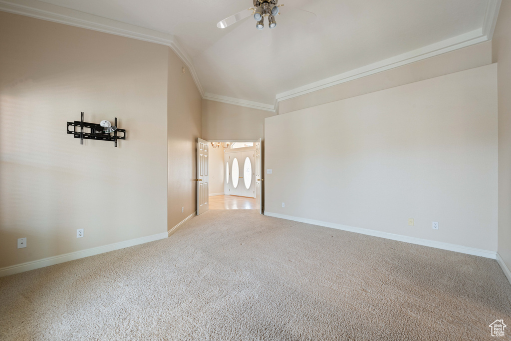 Carpeted spare room with vaulted ceiling, crown molding, baseboards, and ceiling fan