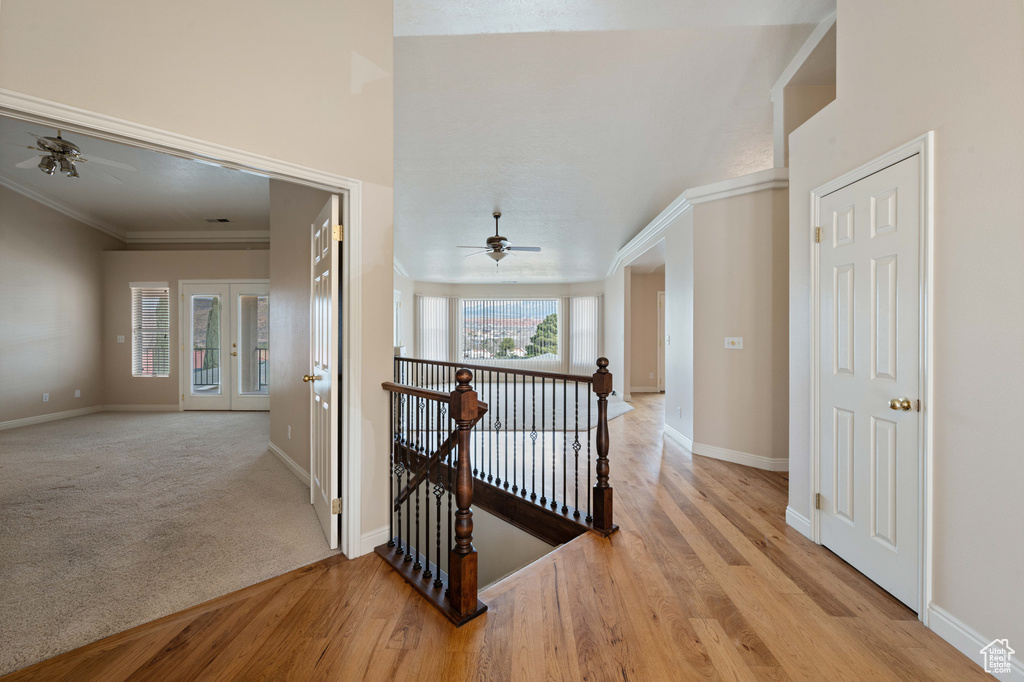 Hallway featuring wood finished floors, baseboards, ornamental molding, french doors, and an upstairs landing