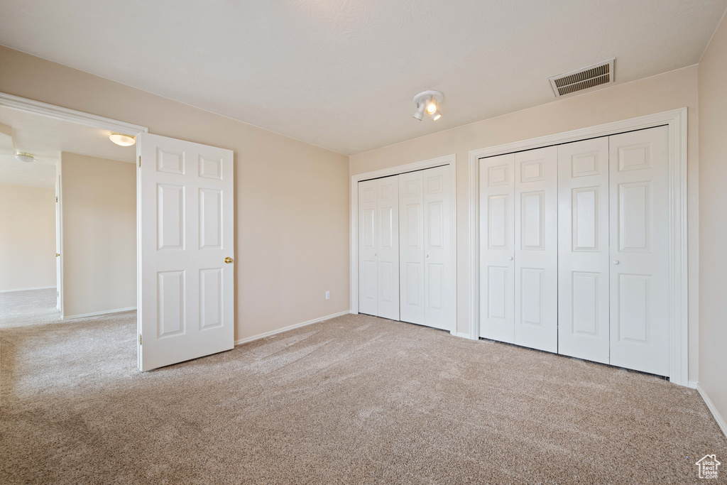 Unfurnished bedroom with visible vents, carpet floors, two closets, and baseboards