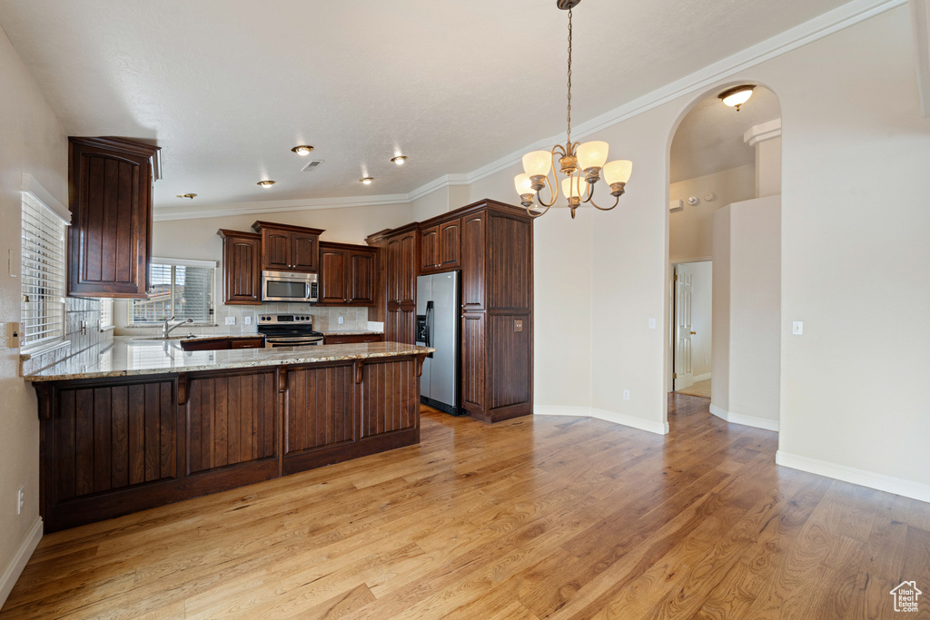 Kitchen with light stone counters, stainless steel appliances, arched walkways, a peninsula, and light wood finished floors