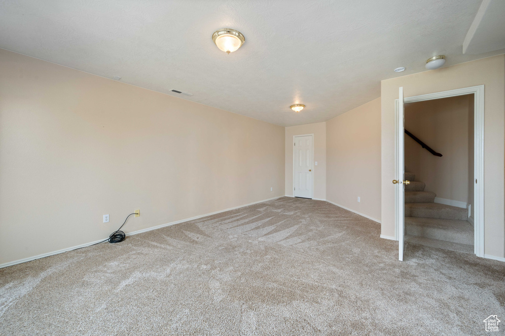 Carpeted spare room featuring stairs, baseboards, and visible vents