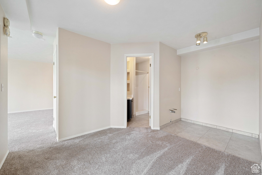 Empty room featuring light tile patterned floors, baseboards, and light carpet