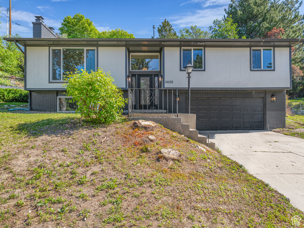 Split foyer home featuring brick siding, an attached garage, concrete driveway, and a chimney