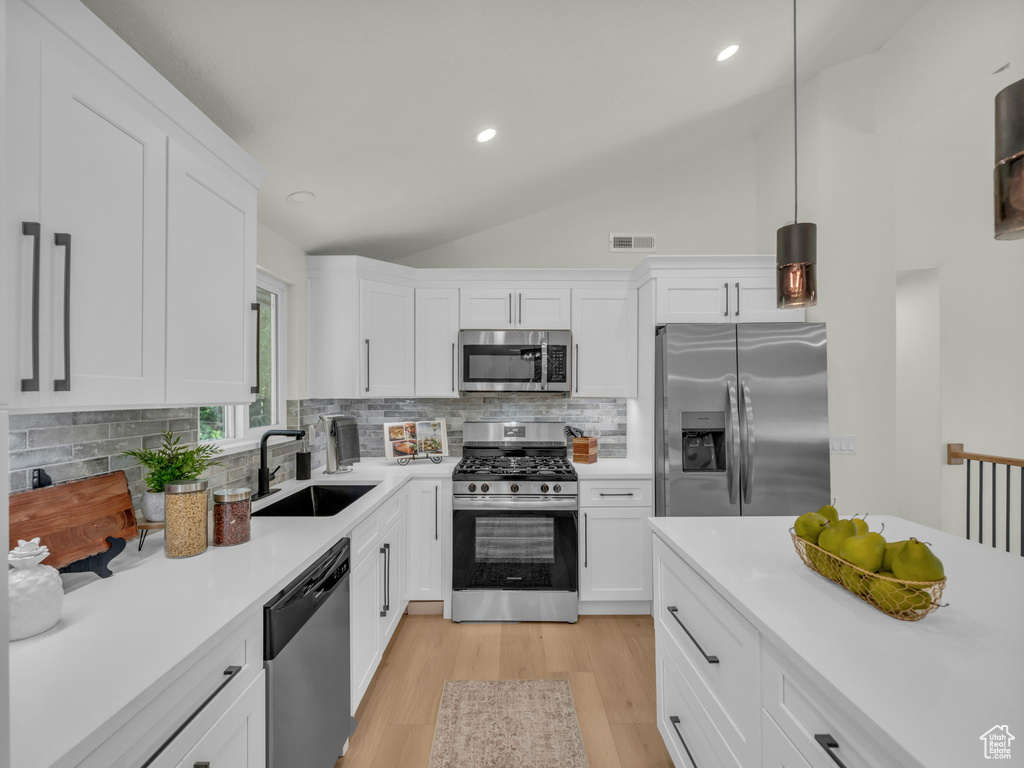 Kitchen featuring appliances with stainless steel finishes, a sink, lofted ceiling, light countertops, and decorative backsplash
