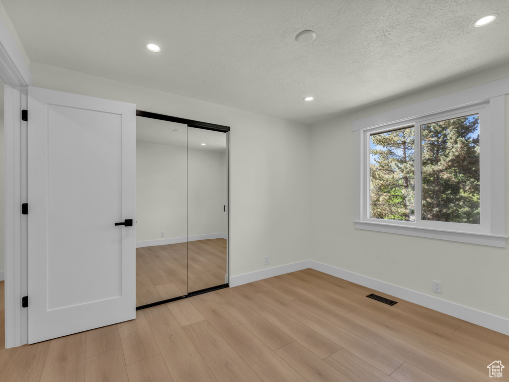 Unfurnished bedroom featuring light wood finished floors, recessed lighting, baseboards, a closet, and a textured ceiling