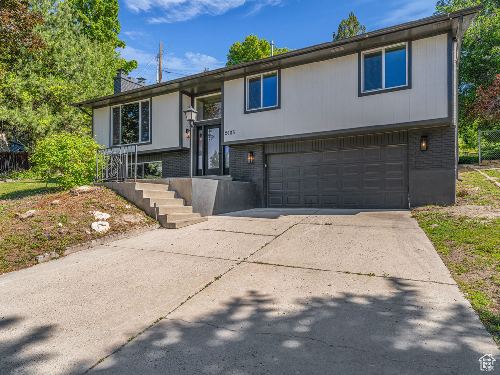 Bi-level home featuring brick siding, an attached garage, a chimney, and driveway