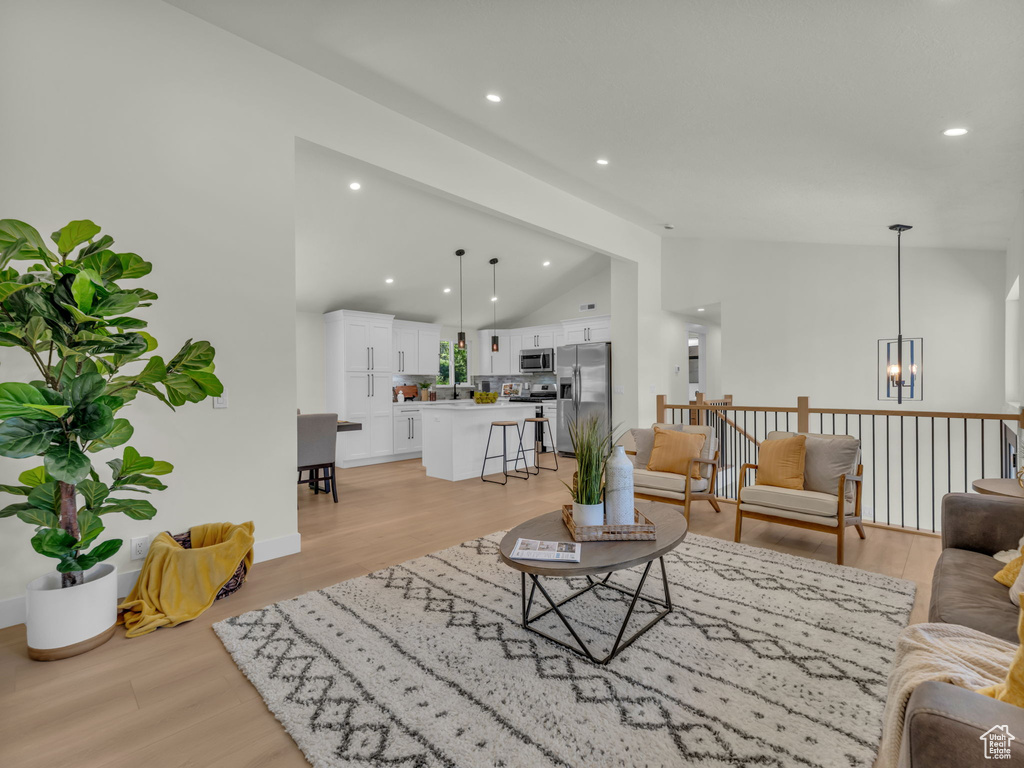 Living area featuring lofted ceiling, a chandelier, recessed lighting, light wood finished floors, and baseboards
