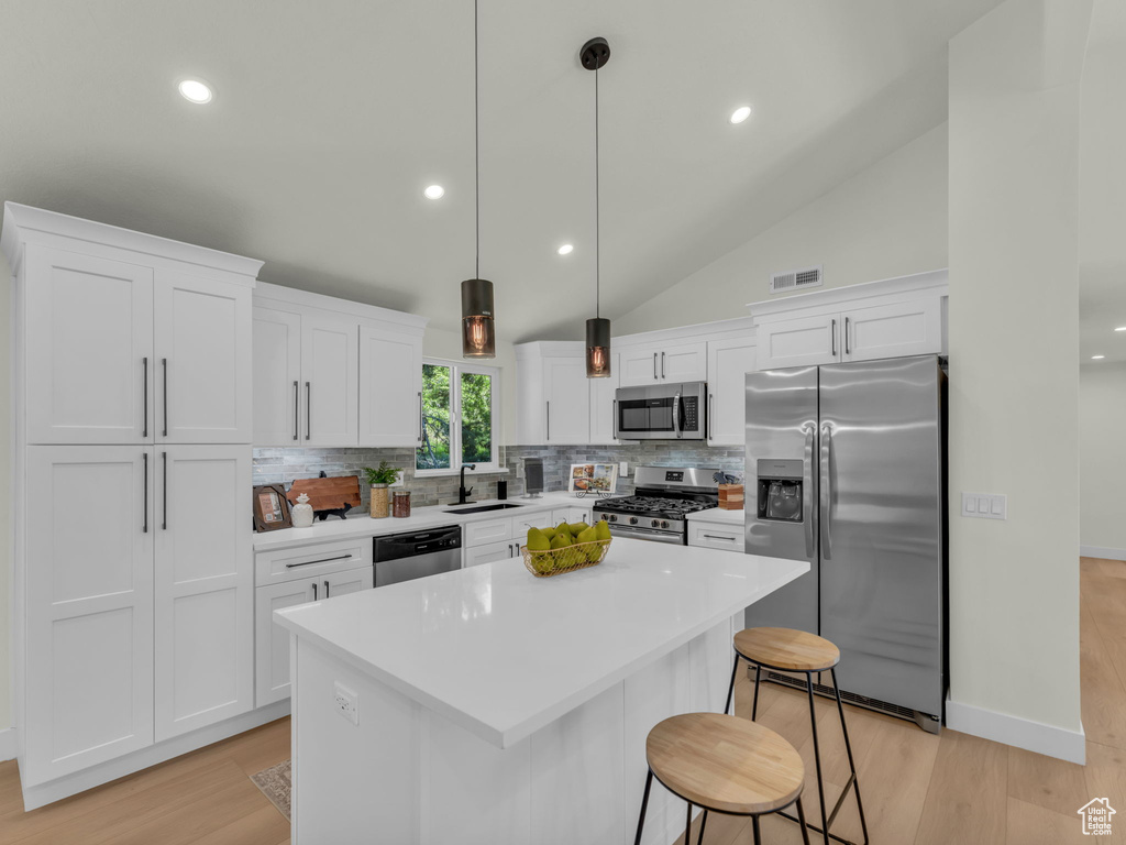 Kitchen with stainless steel appliances, a sink, tasteful backsplash, white cabinetry, and a kitchen island