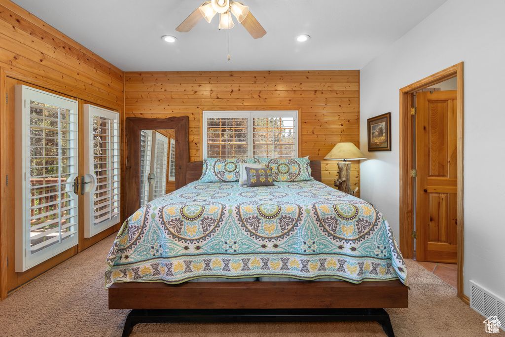 Carpeted bedroom with visible vents, wooden walls, recessed lighting, a ceiling fan, and access to outside