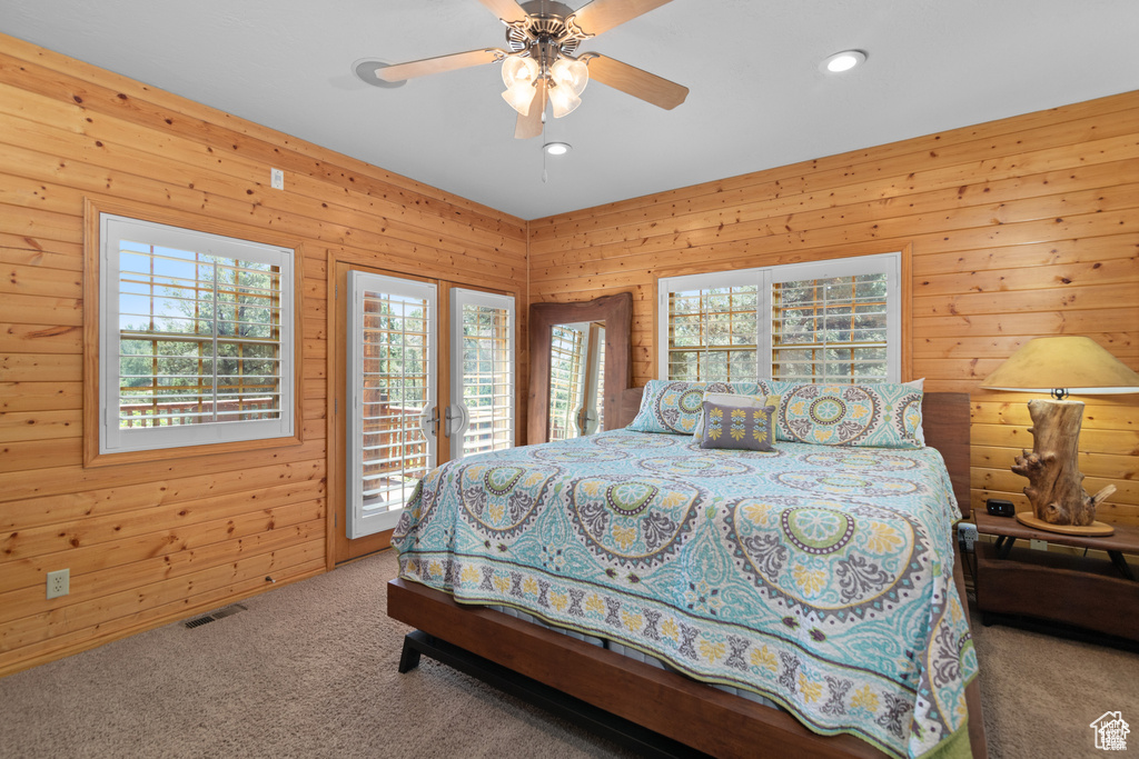 Bedroom with visible vents, access to exterior, wooden walls, carpet flooring, and ceiling fan