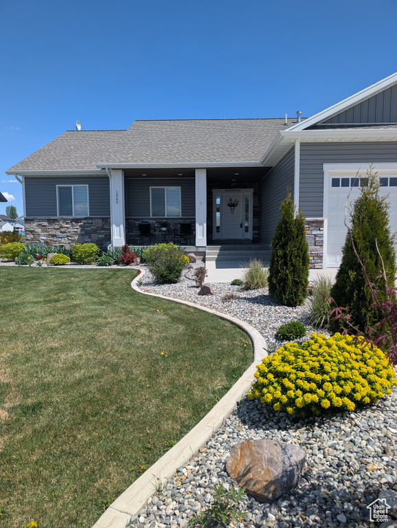 Ranch-style house with stone siding, a garage, a front yard, and roof with shingles