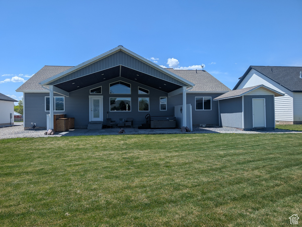 Back of house featuring a patio, a jacuzzi, a yard, a storage shed, and an outbuilding