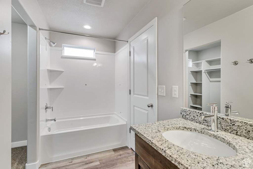 Bathroom with visible vents, a textured ceiling, wood finished floors, washtub / shower combination, and vanity