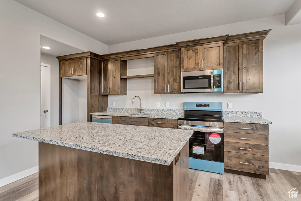 Kitchen featuring light wood finished floors, a center island, baseboards, appliances with stainless steel finishes, and a sink