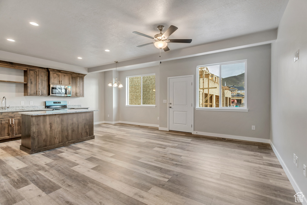 Kitchen with stainless steel appliances, baseboards, light wood-style flooring, and ceiling fan with notable chandelier