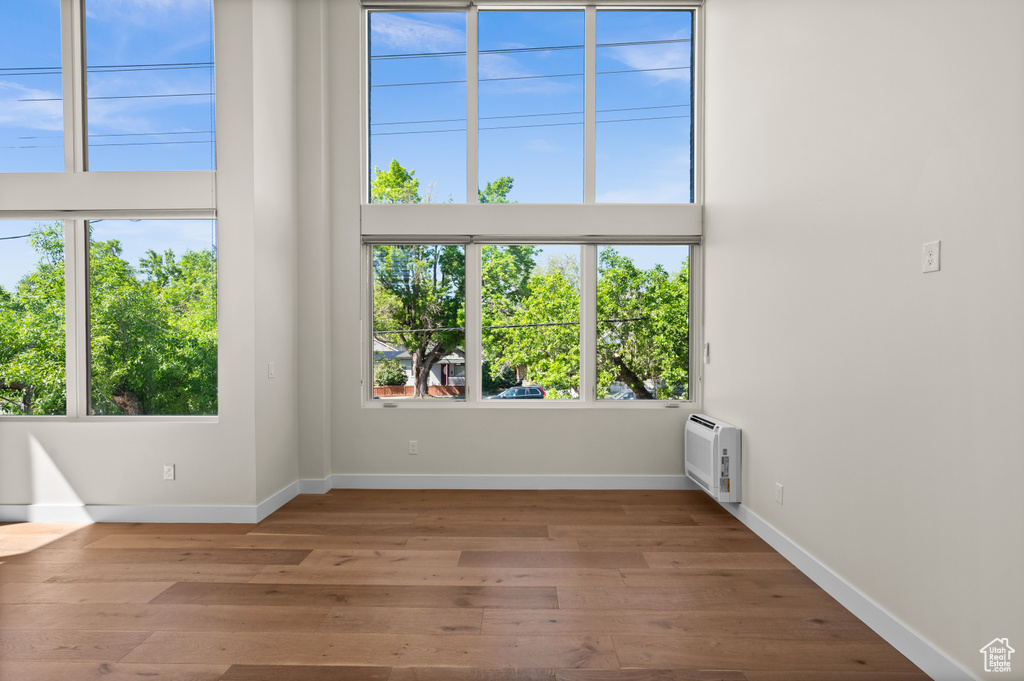 Empty room with plenty of natural light, wood finished floors, baseboards, and heating unit