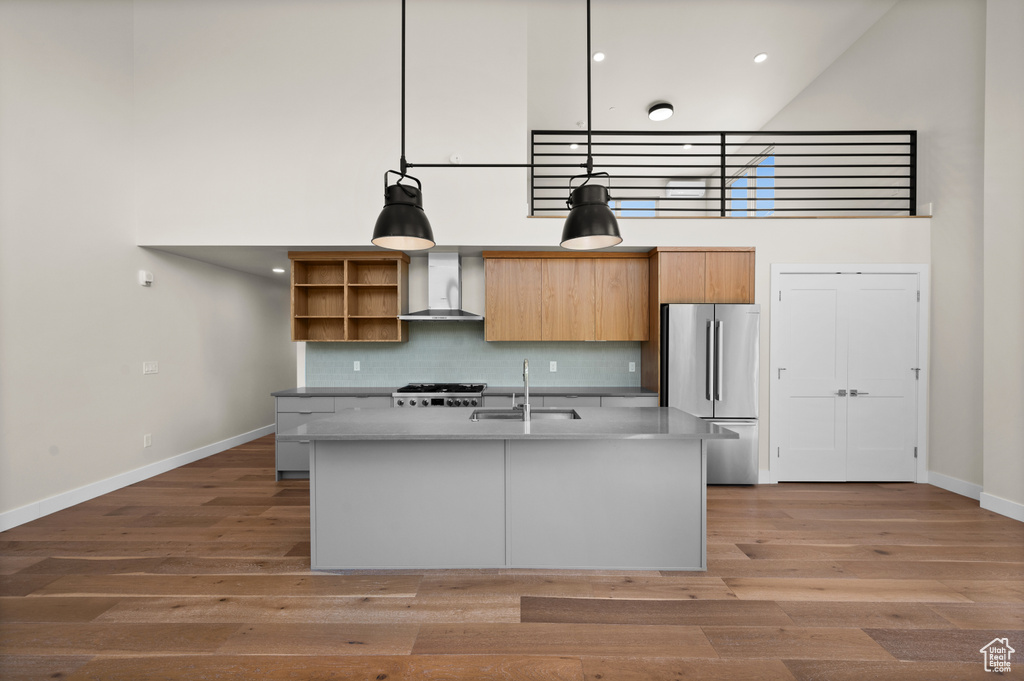 Kitchen with freestanding refrigerator, a towering ceiling, a sink, wall chimney range hood, and baseboards